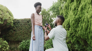 Man proposing to surprised woman in garden, holding engagement ring