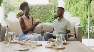African American couple exchanging gifts and smiling while sitting on outdoor sofa