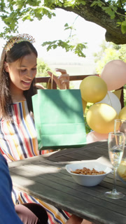 Vertical video: Birthday woman receiving bag from friend and opening gift for celebration on deck