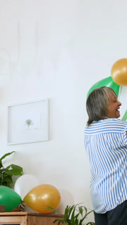 Vertical video: Diverse senior friends preparing birthday at home placing plates arranging balloons