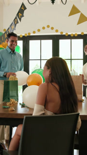 Vertical video: Diverse friends reacting to gift, opening present, laughing around table at home