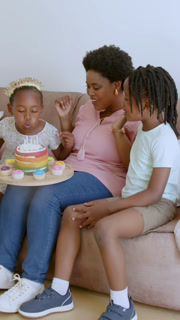 Vertical video: African American family lighting cake candles, opening gift on sofa, copy space
