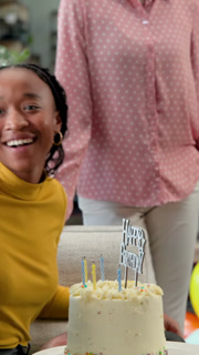 Vertical video: Black woman receiving birthday cake in lounge, clapping and high-fiving coworker
