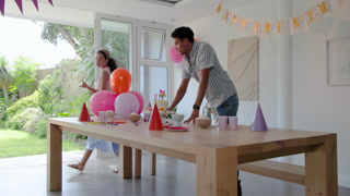 Diverse couple interacting with colorful balloons at home at birthday party, enjoying festive mood