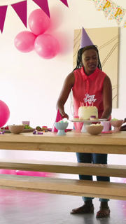 Vertical video: African American family cheering as girl biking indoors, mom cutting birthday cake
