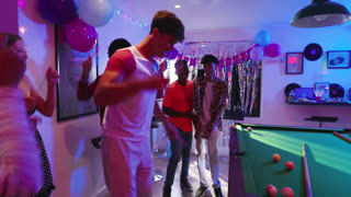 Diverse friends dancing around pool table in game room under disco ball as music plays