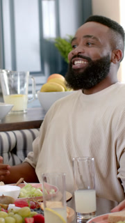 Smiling African American man aged thirty talking at dining table, with lemonade pitcher and fruit