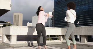 Arriving on rooftop, diverse female friends stretching arms across chest while chatting, warming up