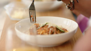 Fork entering frame is puncturing spaghetti in bowl on table, twisting strands and lifting for bite