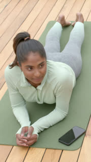 Vertical video: Following smartphone prompt sportswear-clad woman lifting into sphinx pose on deck