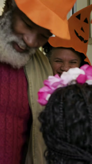 Vertical video: Walking blindfolded blue-caped kid pumpkin pail to porch, adults opening for candy