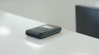 Camera is dollying in, highlighting black keypad device sitting on white desk and reflections