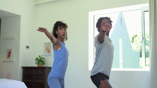 African American couple practicing yoga at home by window, flowing from lunge into prayer for calm
