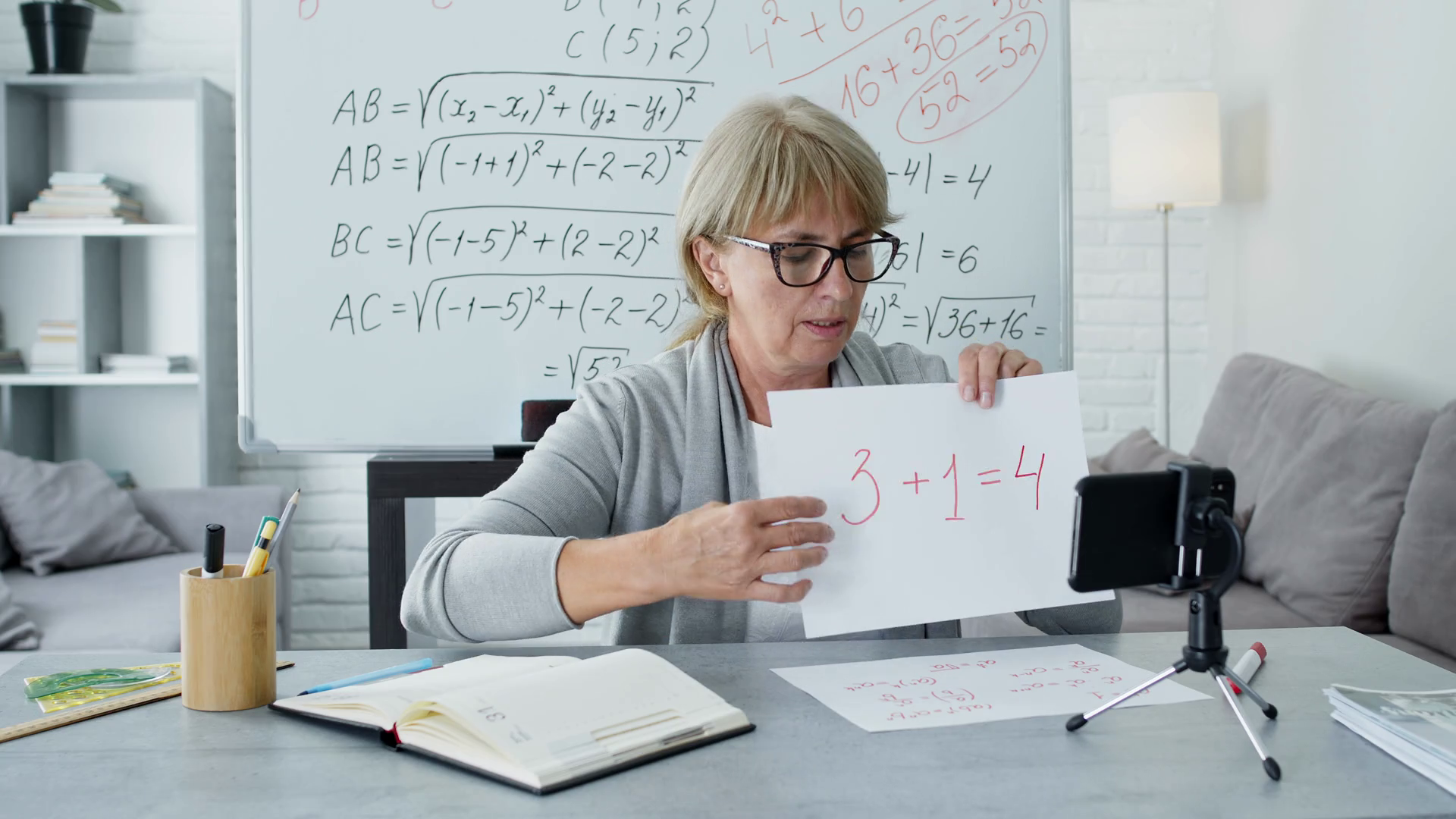 Female Math Teacher Sitting At The Desk. She Conducts An Online Lesson