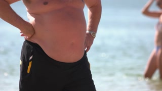 Aged man with belly fat standing on the beach. Obese and unhealthy lifestyle concept.