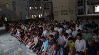 Istanbul, Turkey - 06. 29. 2023: Wide view of a large Muslim congregation sitting in organized rows inside a grand mosque interior. The image
