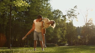 Lovers are walking in the park at sunset. The girl is on the boy's back, they are having fun and circling.