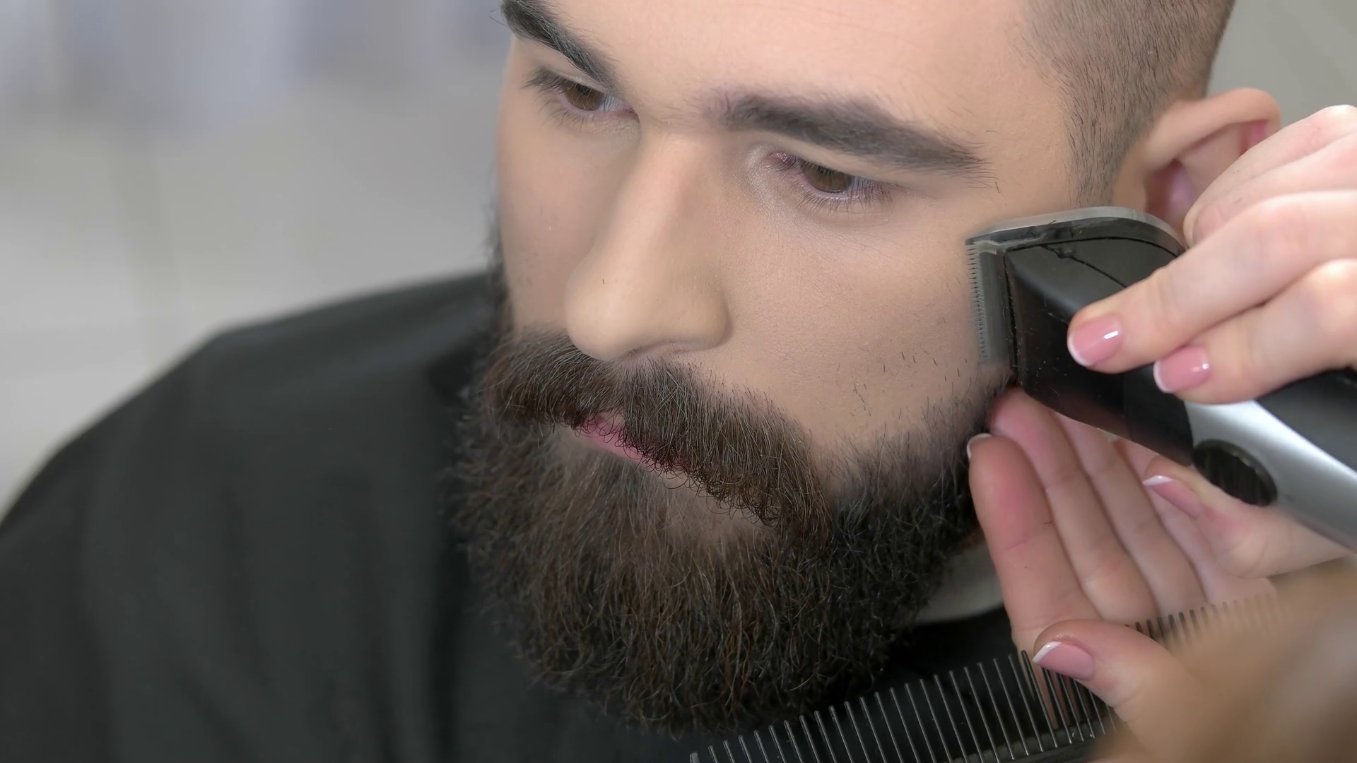 Beard grooming process, close up. Barber using trimmer and comb. Stock