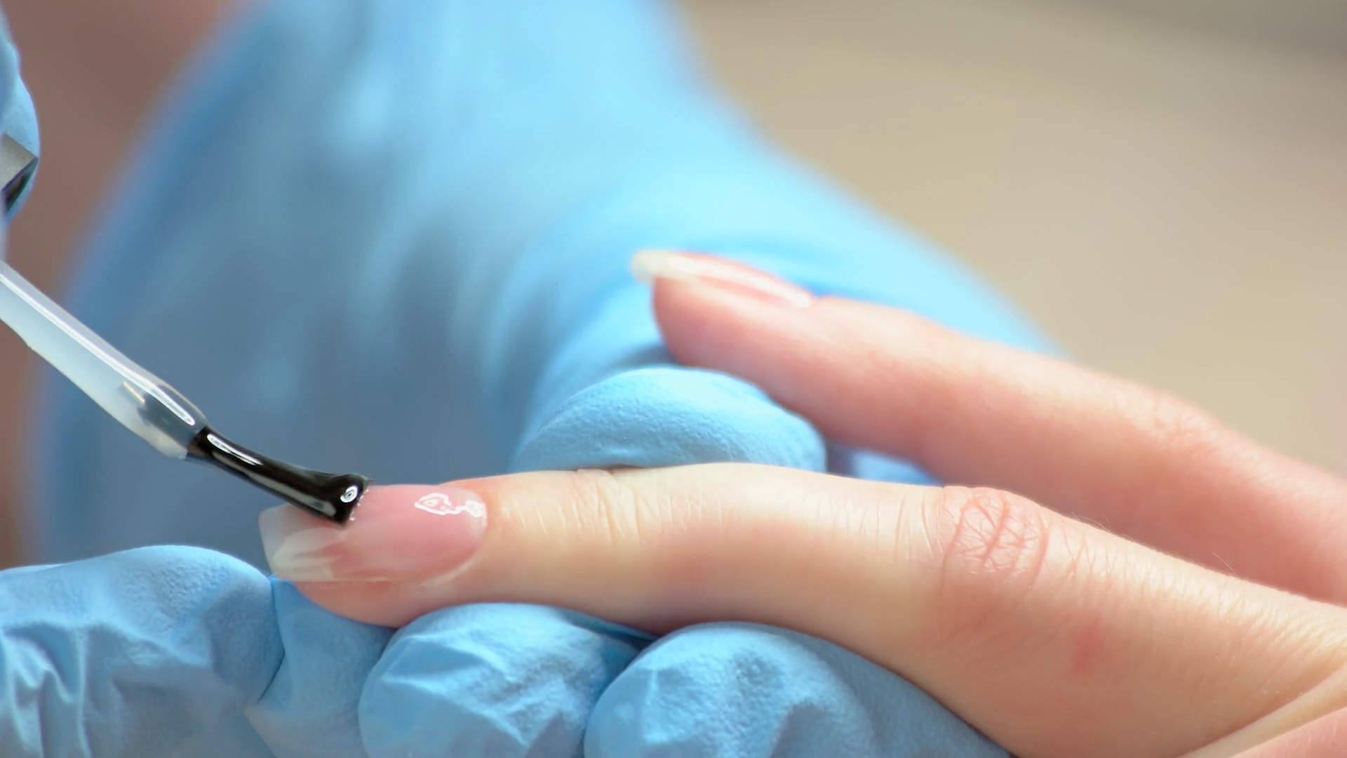 Close up process of polish applying on nail. Nail beautician in blue