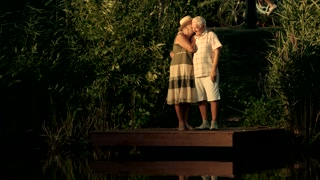 Elderly couple kissing near water. Old man pointing with finger distance on summer nature background. Leisure of senior couple.