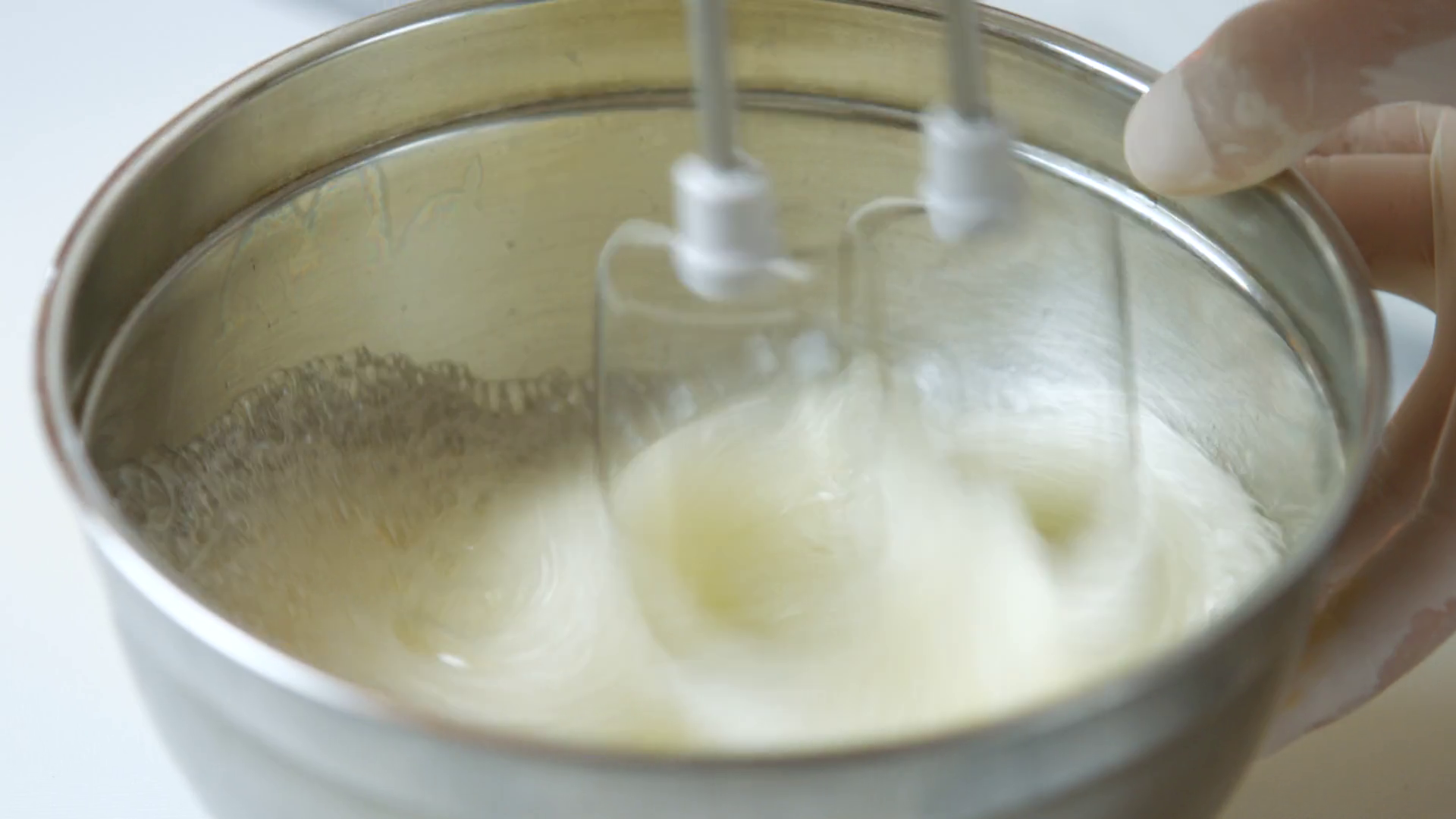 Electric mixer beats egg. Hand holds bowl under mixer. Chicken egg for