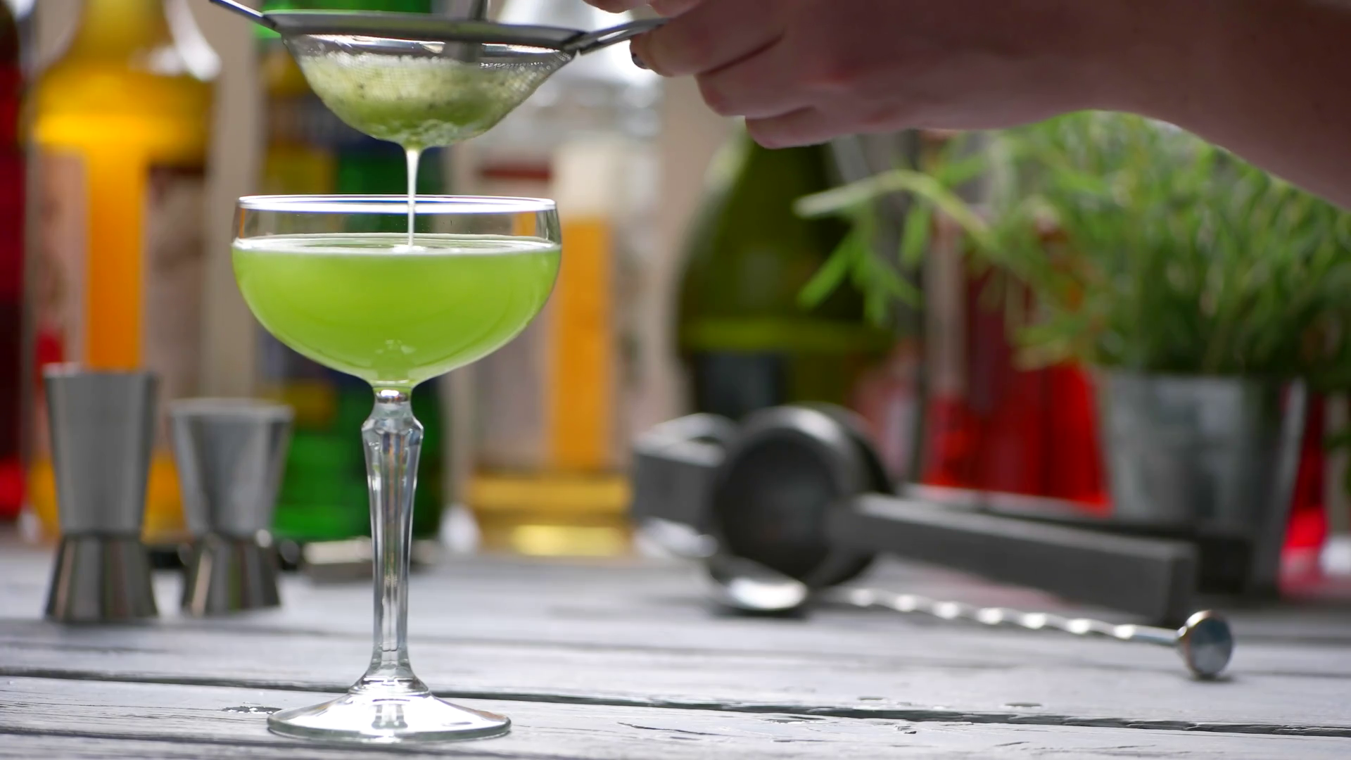 Green drink drips through sieve. Hands with sieve and spoon. Bartender prepares kiwi daiquiri