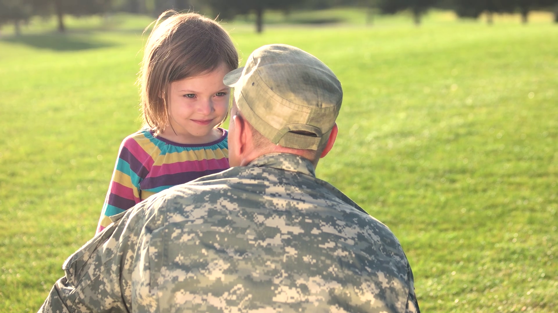 Soldier in camoubackgrounde hugging his daughter in the park. Caucasian