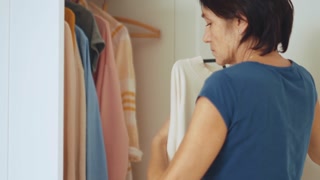 Concentrated brunette woman hangs clothes in closet at home