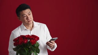 Angry man holding bouquet and typing by phone