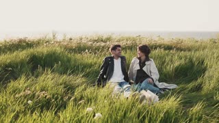 Friendly couple talking while sitting on picnic blanket on field by sea