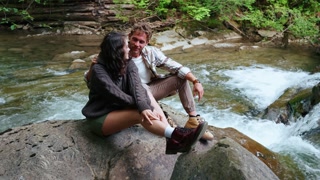 Couple hugging and looking at view on rock by mountain river