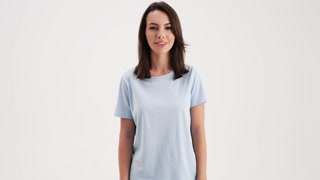 A beautiful woman wearing basic t-shirt is looking to the camera standing in the studio isolated over white background