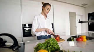 Cheerful pretty blonde woman cooking vegetables while standing on kitchen at home