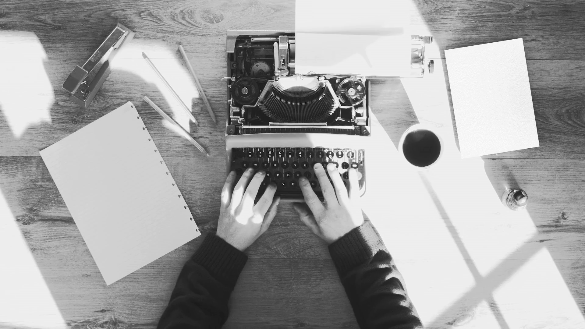 Black and white from above shot of hands typing on a vintage typewriter