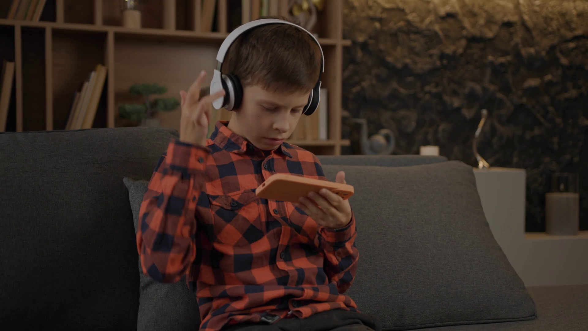Kid with autism using mobile phone wearing headphones sitting on couch at home. Stock Video