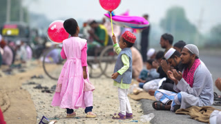 Bogura, Bangladesh - 14 April 2024: View of children playing with balloons while men offer prayers on the roadside during Eid celebrations.