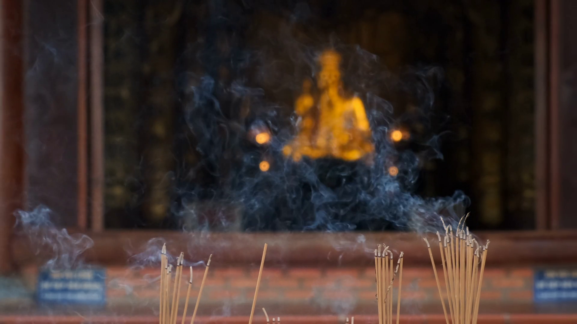 Smoking incense sticks in stone altar against golden statue in buddhist