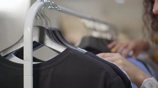 Woman is looking for t-shirt on rack in clothing store, close-up of her hands