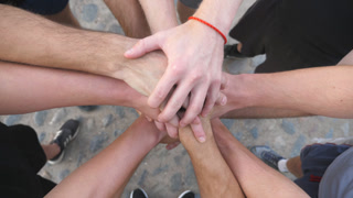 Top view hands of young athletes stacking together one by one in unity. Group of best friends putting their arms in centre of a circle and raising them up. Concept of friendship and teamwork. Slow mo.
