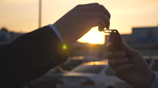 Male hands giving keys of car to his friend with sun flare at background. Arm of businessman passed car key. Handshake between two business men outdoor. Close up Slow motion