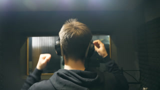 Male singer in headphones singing song at sound studio. Unrecognizable young man emotionally recording song. Working of creative musician. Show business concept. Slow motion Rear back view