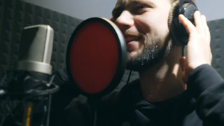 Male singer in headphones singing song into the microphone at sound studio. Young man emotionally recording new melody or song. Working of creative musician. Show business concept. Slow motion.