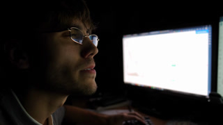 Focused trader analyzing cryptocurrency market trends on computer screen, illuminated by soft monitor light, showcasing intense