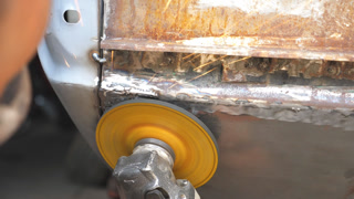 Male hands of welder grinding old car body using grinder machine and protective eyewear in workshop. Arms of repairman or mechanic worker