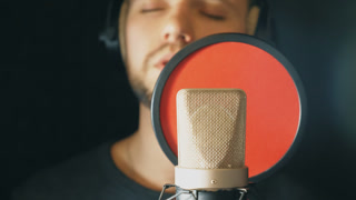 Male singer in headphones singing in sound studio. Young man emotionally recording new song. Guy sings to microphone. Working of creative musician. Show business concept. Slow motion Close up