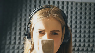 Portrait of beautiful girl singing in sound studio. Young singer emotionally recording new song. Lady sings to microphone. Working of creative musician. Show business concept. Slow motion Close up