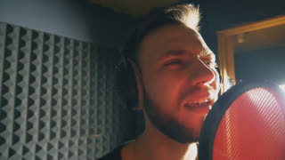 Portrait of young singer singing in sound studio. Handsome man emotionally recording new song. Guy sings to microphone. Working of creative musician. Show business concept. Slow motion Close up