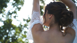 Young attractive bride in white dress with bare back posing on camera in rays of sun. Happy beautiful woman enjoying nature or wedding day outdoor. Concept of marriage. Slow motion Close up.