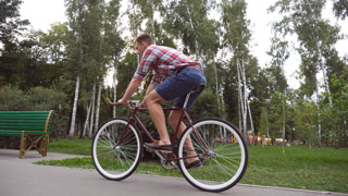 Follow to young handsome man riding a vintage bicycle outdoor. Sporty guy cycling at the park. Healthy active lifestyle. Side view Close up Slow motion.