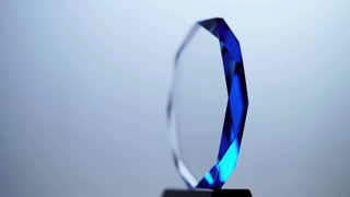 Blue crystal glass trophy award spinning on black base against gradient background for achievement recognition success winner ceremony corporate honors prize ceremony